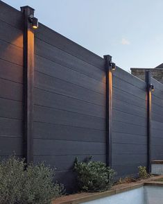 an outdoor swimming pool next to a tall fence with lights on it's sides