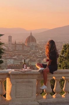 a woman sitting on top of a balcony next to a bottle of wine