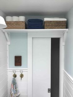 a white bathroom with blue walls and towels on the shelf above the door is a towel rack