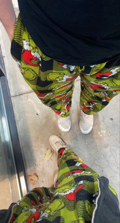 a person standing next to an escalator wearing green and red patterned pants with white shoes