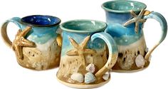 three ceramic mugs with starfish and seashells on them, one is blue