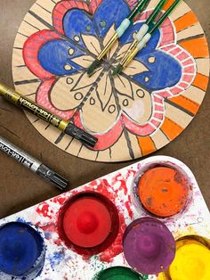 the paint and brushes are sitting on the table next to the paper plate that is decorated with flowers