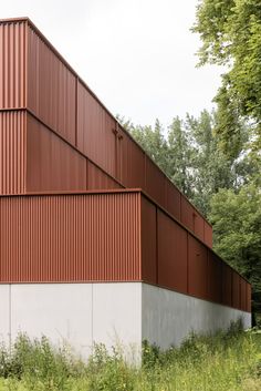 the side of a building that is made out of red metal and white walls with trees in the background