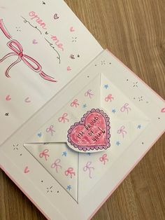 an open card with a heart and bow on the inside is sitting on a table