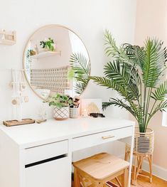 a white desk topped with a mirror next to a potted plant and wooden stool