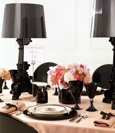 the table is set with black and white plates, silverware, and pink flowers