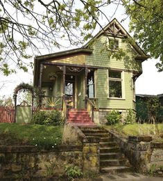 a green house with steps leading up to it's front door and stairs going up to the second floor