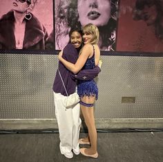 two young women hugging each other in front of pictures on the wall and behind them