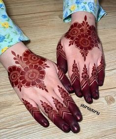 two hands with henna designs on them sitting on a wooden table next to each other