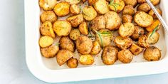 cooked potatoes in a white dish with a spoon on the side and green herbs sprinkled on top