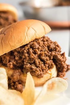 a close up of a sandwich and some chips on a plate with food in the background