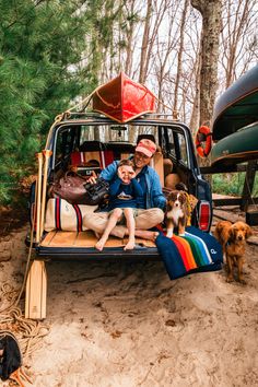 a man and woman sitting in the back of a truck with two dogs next to it