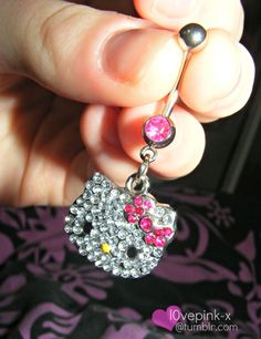 a person holding onto a hello kitty belly ring with pink and yellow crystals on it