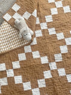 a teddy bear laying on top of a brown and white checkerboard bed spread