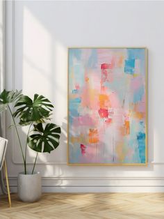 an abstract painting hangs on the wall next to a potted plant in a white room