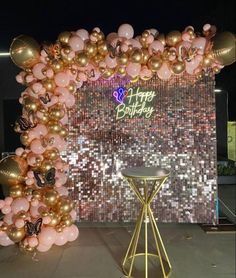 a balloon arch with pink and gold balloons in front of a happy birthday sign on the wall