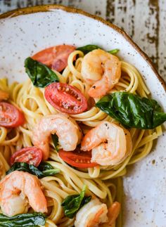 pasta with shrimp, tomatoes and spinach in a white bowl on a wooden table