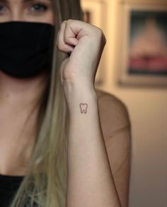 a woman wearing a black mask and holding her arm up to the camera with a tooth tattoo on it