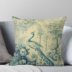 a blue and yellow peacock sitting on top of a couch next to a white pillow