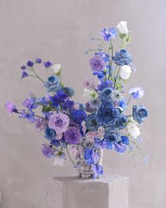 a vase filled with blue and white flowers sitting on top of a cement block next to a wall