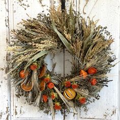 a wreath with dried flowers and oranges is hanging on a white wooden door,