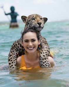 a woman in the water with a leopard on her shoulders, and another person behind her