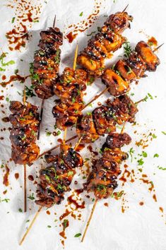 chicken skewers with barbecue sauce and garnishes on a white surface