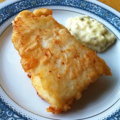 a piece of fried fish on a blue and white plate next to mashed potatoes