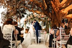 a bride and groom standing under a tree at their wedding ceremony in front of an audience