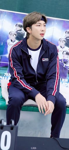 a young man sitting on top of a bench next to a wall with a poster behind him