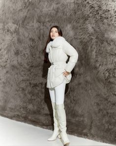 a woman standing in front of a fur wall wearing white boots and a long coat