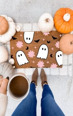 a person holding a cup of coffee in front of a door mat with ghost faces on it