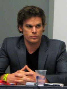 a man sitting at a table in front of a cup with his hands folded out