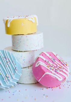 three different colored donuts with sprinkles and white frosting on them