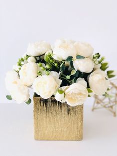 white flowers are in a gold vase with greenery