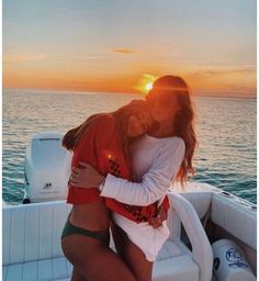 two women hugging on the back of a boat in the ocean at sunset or sunrise