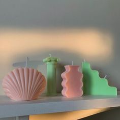 three candles sitting on top of a shelf next to a vase and seashells