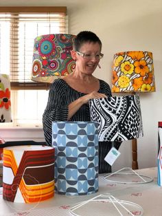 a woman standing next to some lamps and boxes on a table with other items in front of her