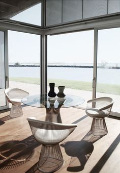 a glass table with chairs and vases on it in front of a large window