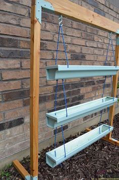 a wooden swing with two benches attached to it in front of a brick wall and mulch