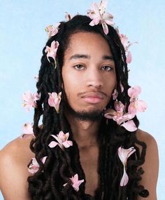 a man with long dreadlocks and pink flowers on his hair is looking at the camera