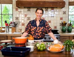 a woman standing in the middle of a kitchen with lots of food on the counter