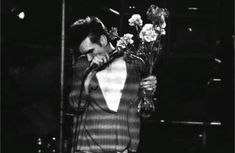 a man in a suit and tie holding flowers while standing next to a microphone on stage