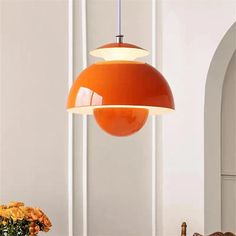 an orange pendant light hanging over a dining room table with flowers in the foreground