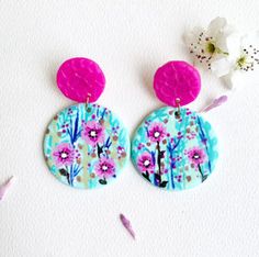 two pink and blue earrings with flowers on the bottom one has a flower in front of it