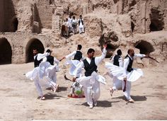 several men in white and black clothing dancing on the sand with their arms spread out