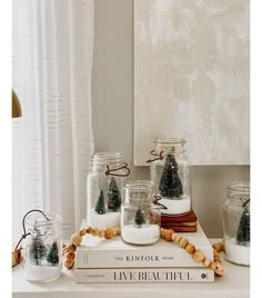 a table topped with jars filled with candles and snow covered pine trees on top of books