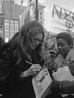 black and white photograph of two women writing in front of a protest sign on the street