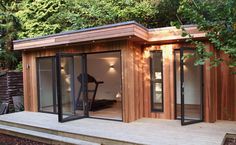 a small wooden building with glass doors on the front and side windows, sitting next to trees