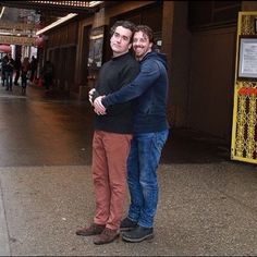 two people standing next to each other in front of a building